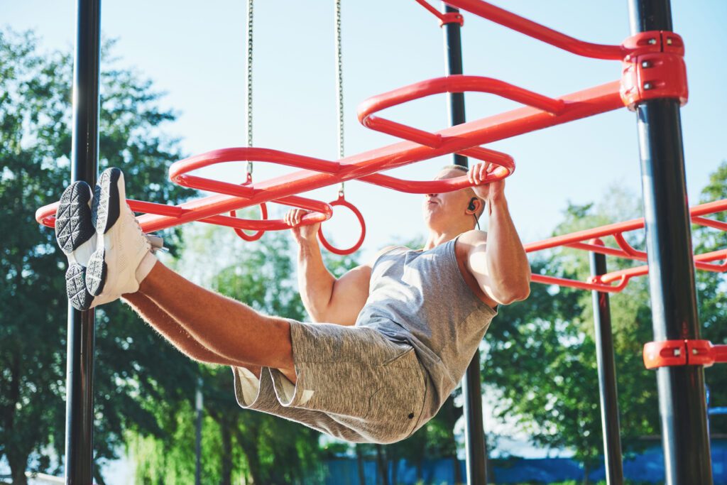 Muscular man with beautiful torso exercising on horizontal bars on a blurred park background. Young man doing pull-ups outdoors.